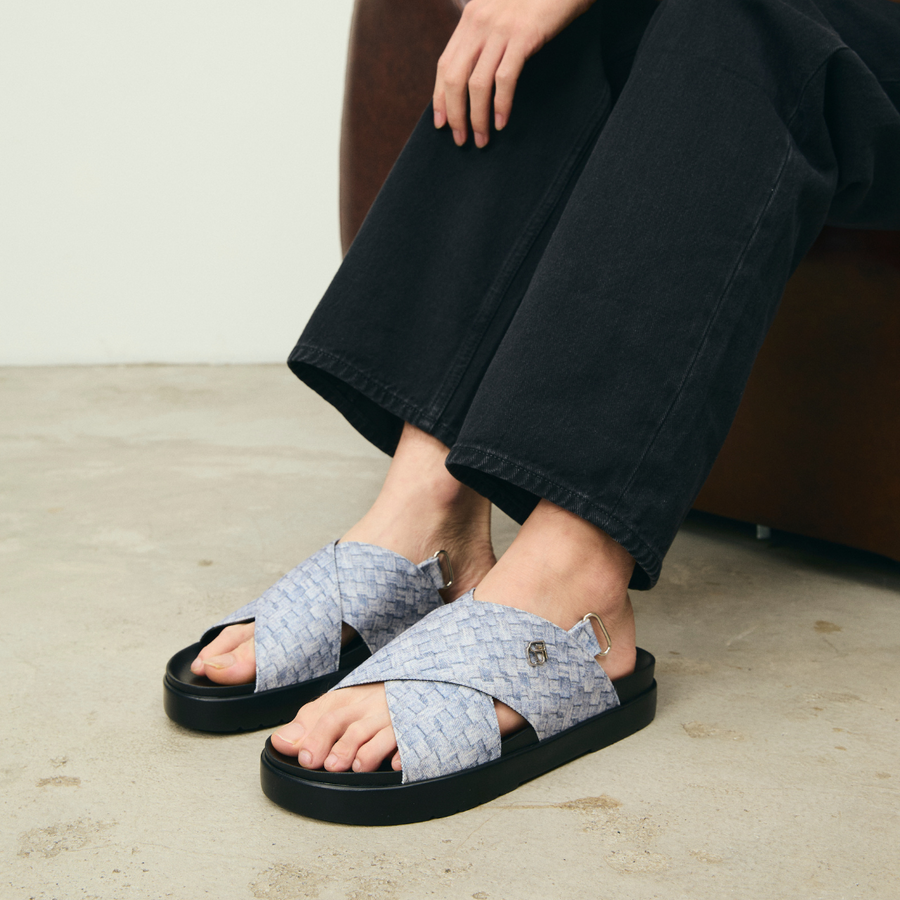 Person wearing woven sandals with black soles on a neutral background